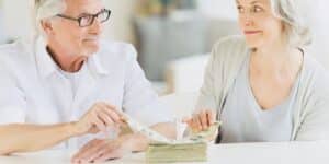 An elderly couple looks concerned while holding a stack of money and documents, symbolizing financial stress and anxiety.